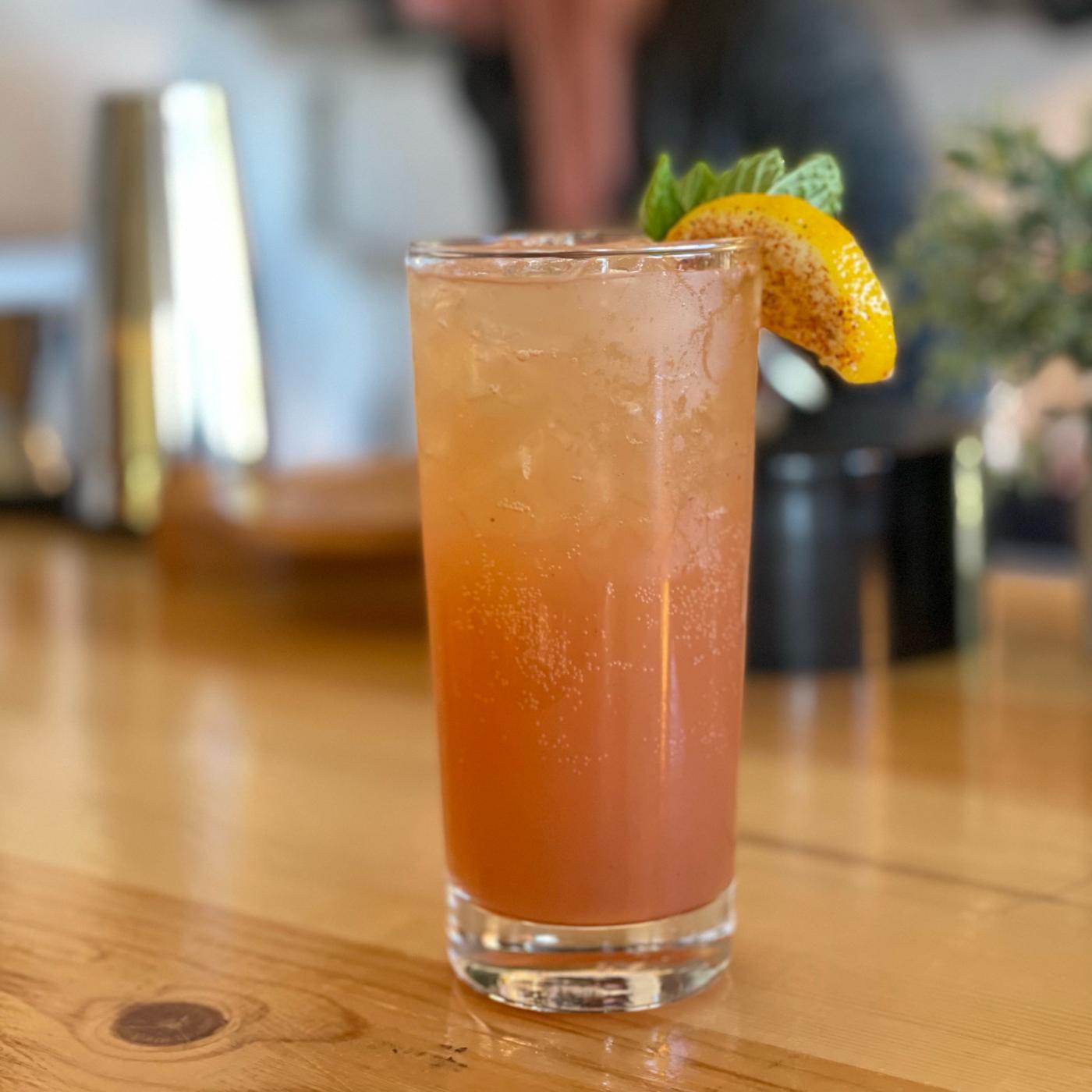 A tall signature cocktail garnished with lemon and mint