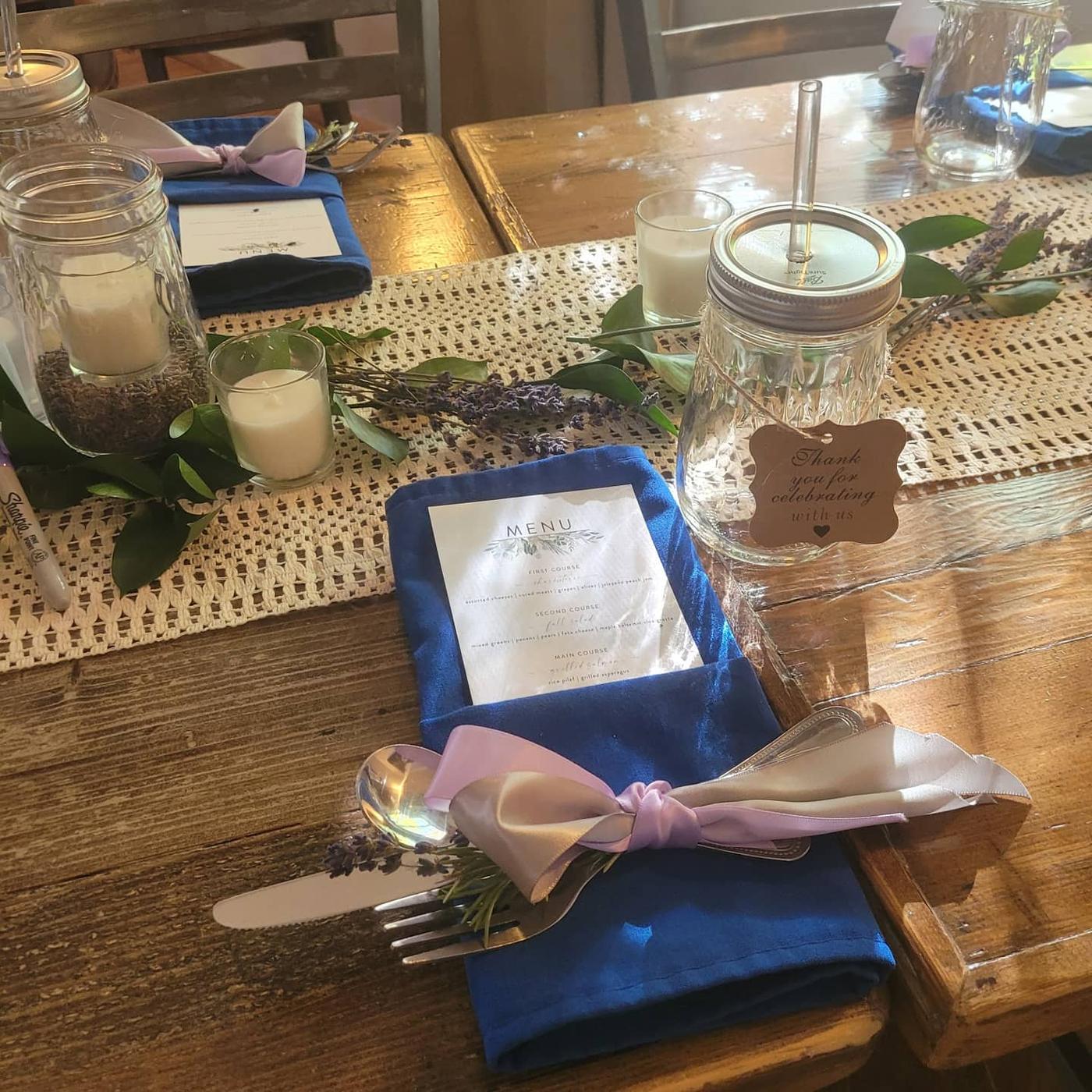 A long wood table set with royal-blue napkins, candles and lavender for a private celebration